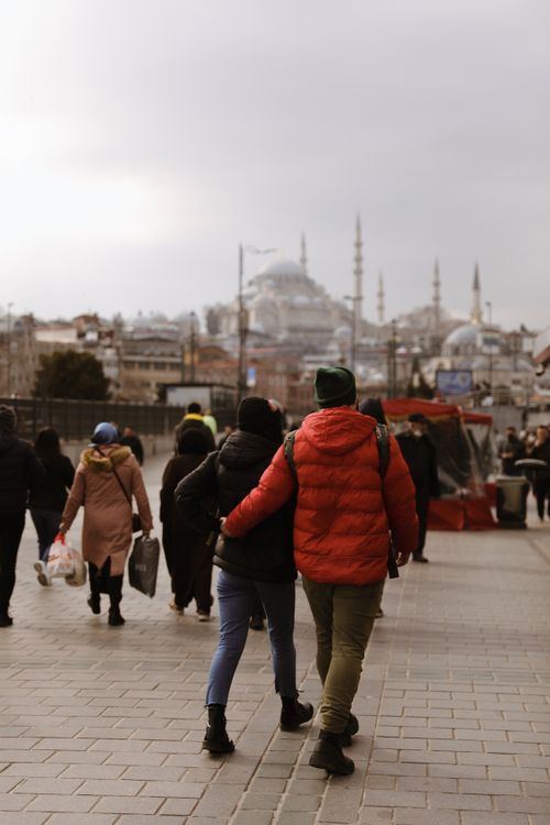 Free A couple walks on a city street with iconic mosques in the background on a cloudy day. Stock Photo