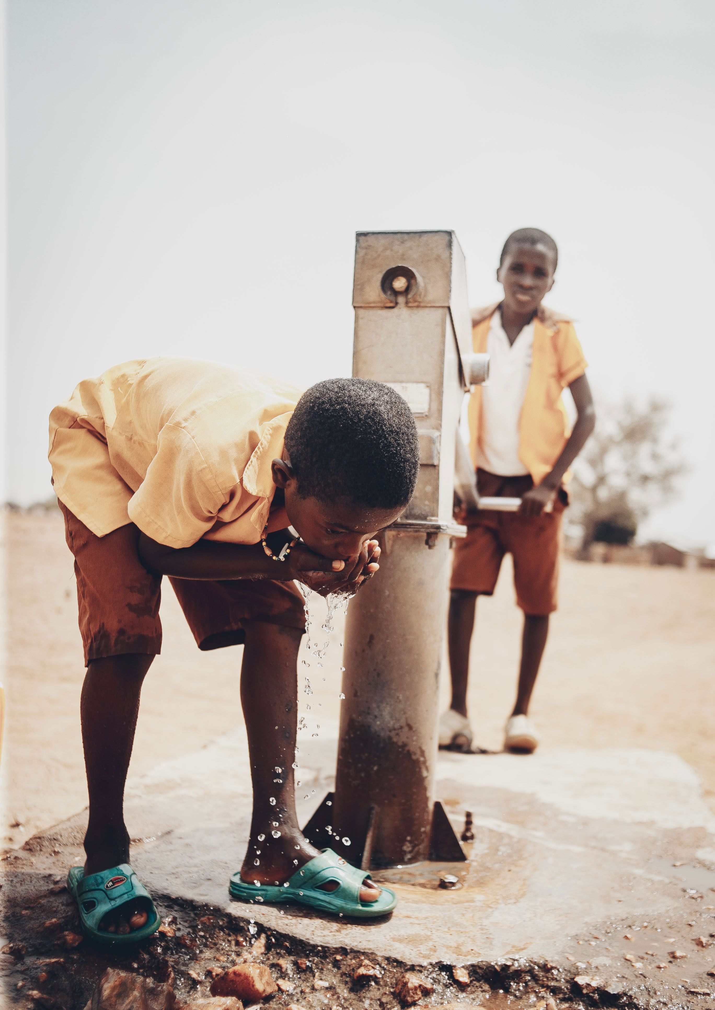 Two boys enjoying fresh water from a pump on a sunny day.