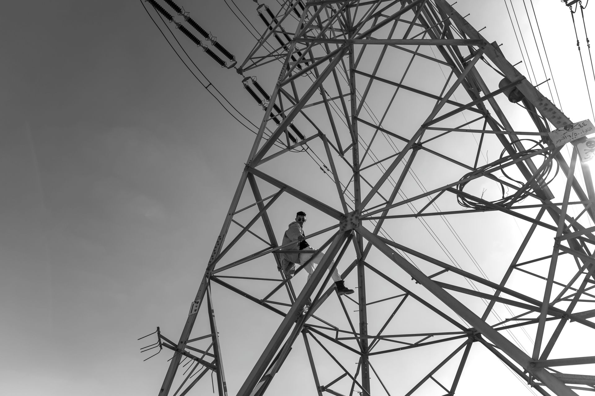 A black and white photo of a man climbing up a high power tower