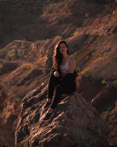 Free A young woman sits peacefully on a rock formation, enjoying a summer day outdoors. Stock Photo