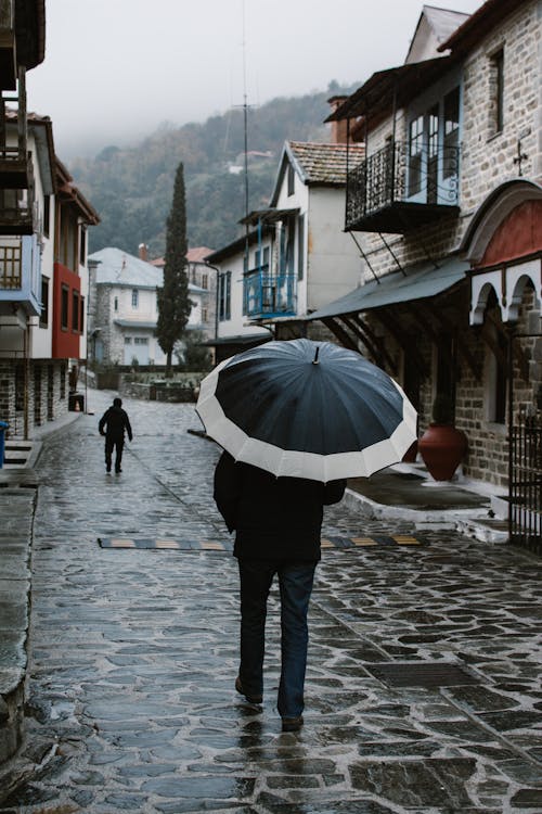 Person with Umbrella on Cobblestone Street in Town