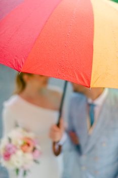A couple embraces under a vibrant umbrella, sharing a moment in the rain.