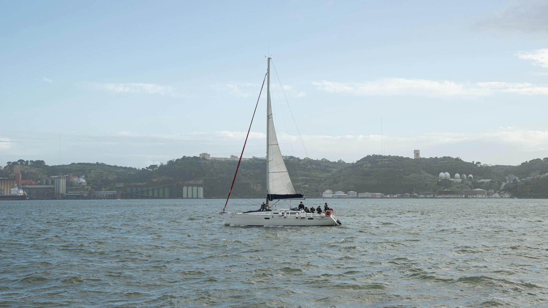 Sailboat cruising on a serene river with Lisbon's scenic landscape in the background.