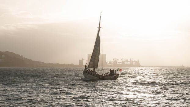 A sailboat glides on a shimmering Lisbon sea with a hazy skyline in the background.