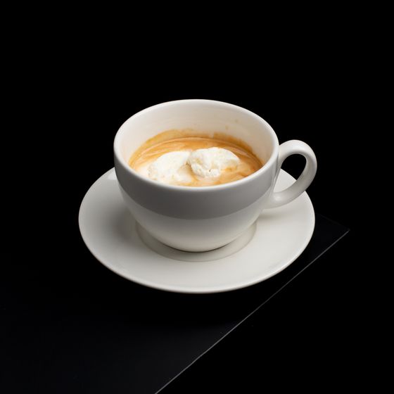 White cup and saucer holding hot espresso with a melting scoop of vanilla gelato on black