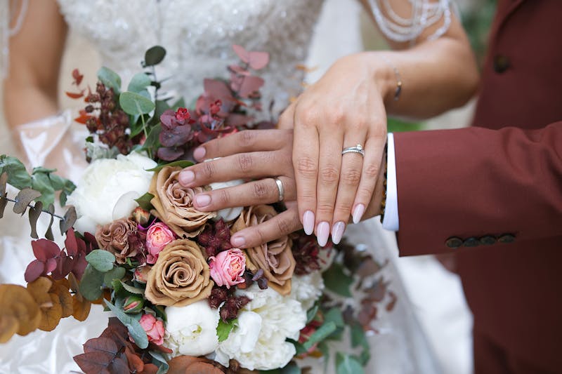 Main des mariés sur un bouquet de fleurs, mettant en avant leurs alliances.