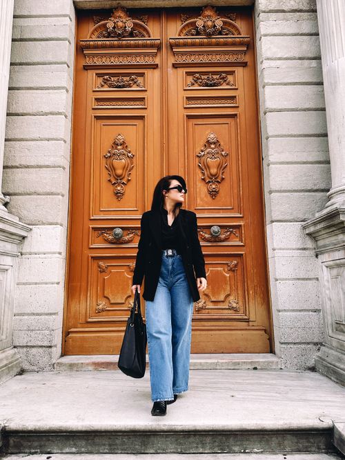 Free Fashionable woman stands confidently before an ornate wooden door, exuding elegance and style. Stock Photo