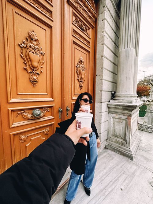 Free Stylish person enjoying coffee in front of ornate wooden doors in a city setting, adding to urban charm. Stock Photo