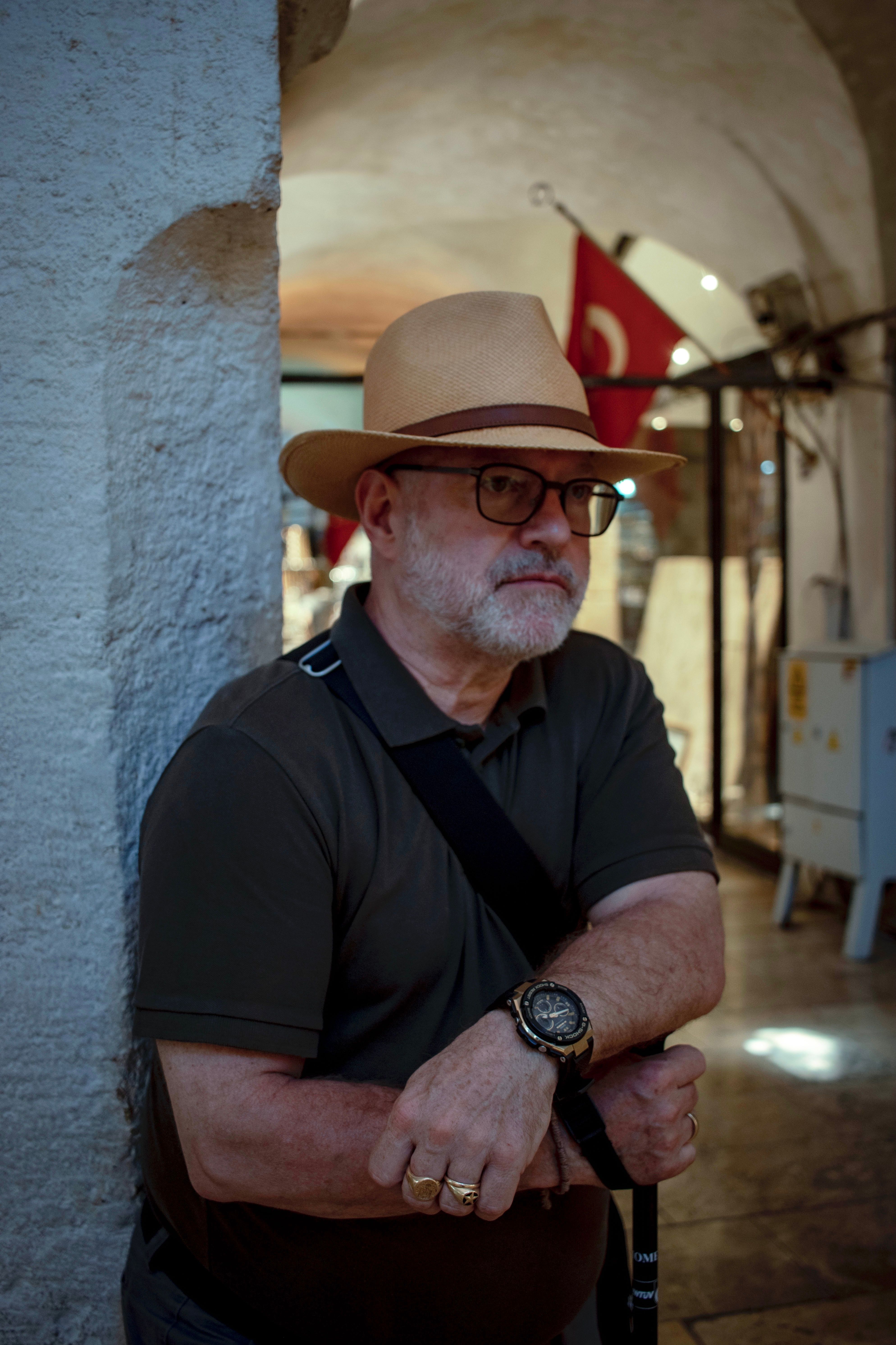 Senior man with hat and glasses standing in an indoor archway.