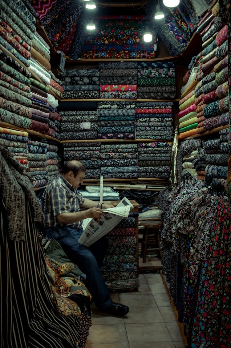 Man Reading Newspaper In Store With Fabrics