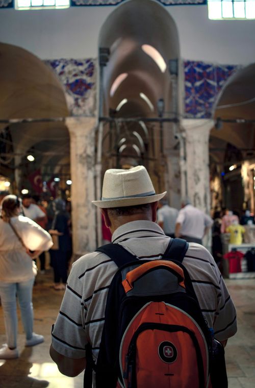 Free A man with a hat and backpack explores a vibrant indoor market filled with people. Stock Photo