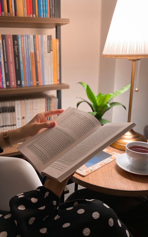 Woman Sitting by the Table and a Lamp Reading a Book 