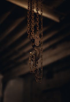 A detailed view of a rusty chain and hook with a blurred industrial background.