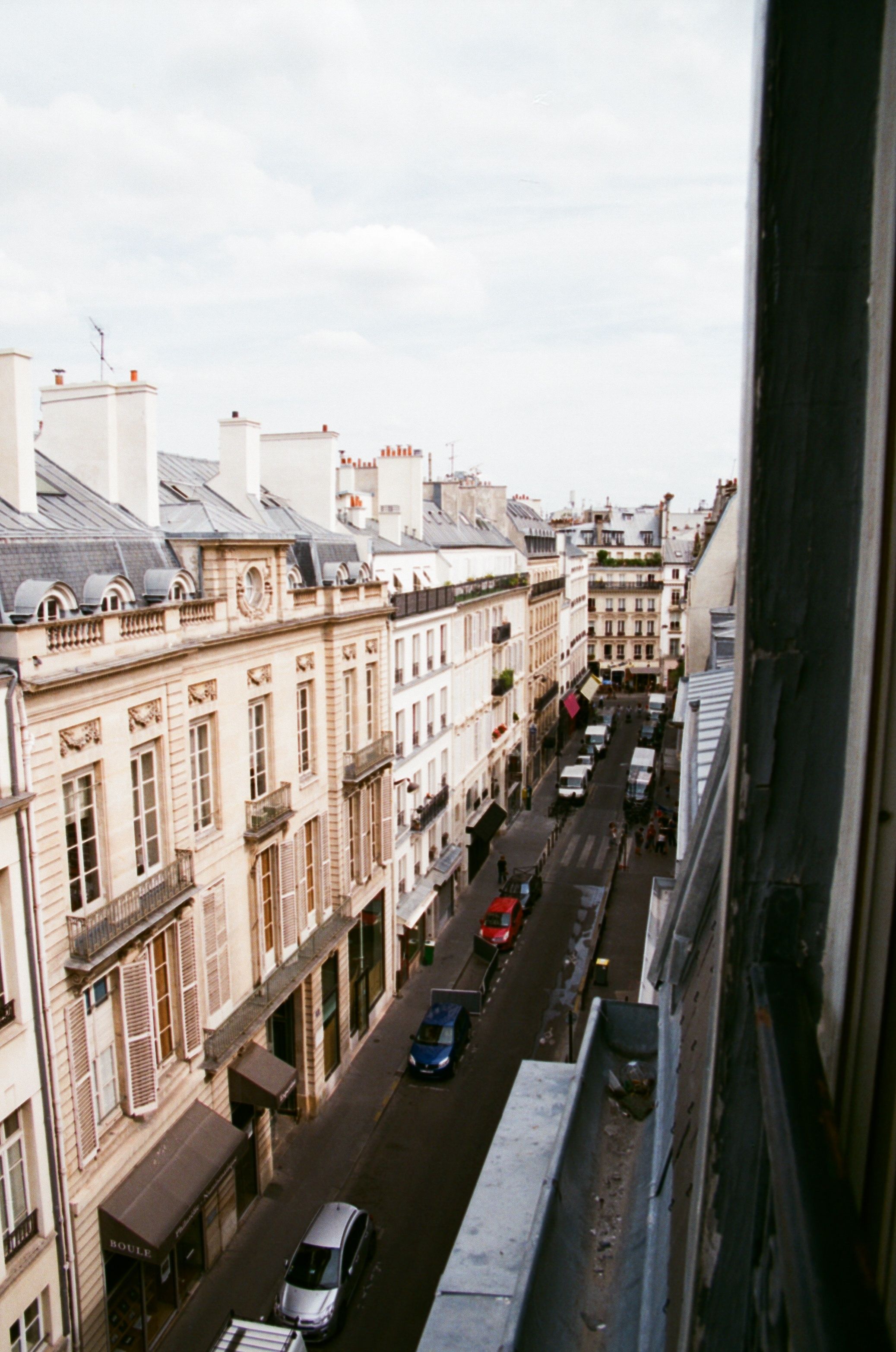 Captured from a window, this image showcases a classic Parisian street with historic buildings.