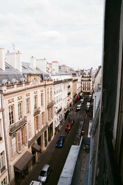 Captured from a window, this image showcases a classic Parisian street with historic buildings.