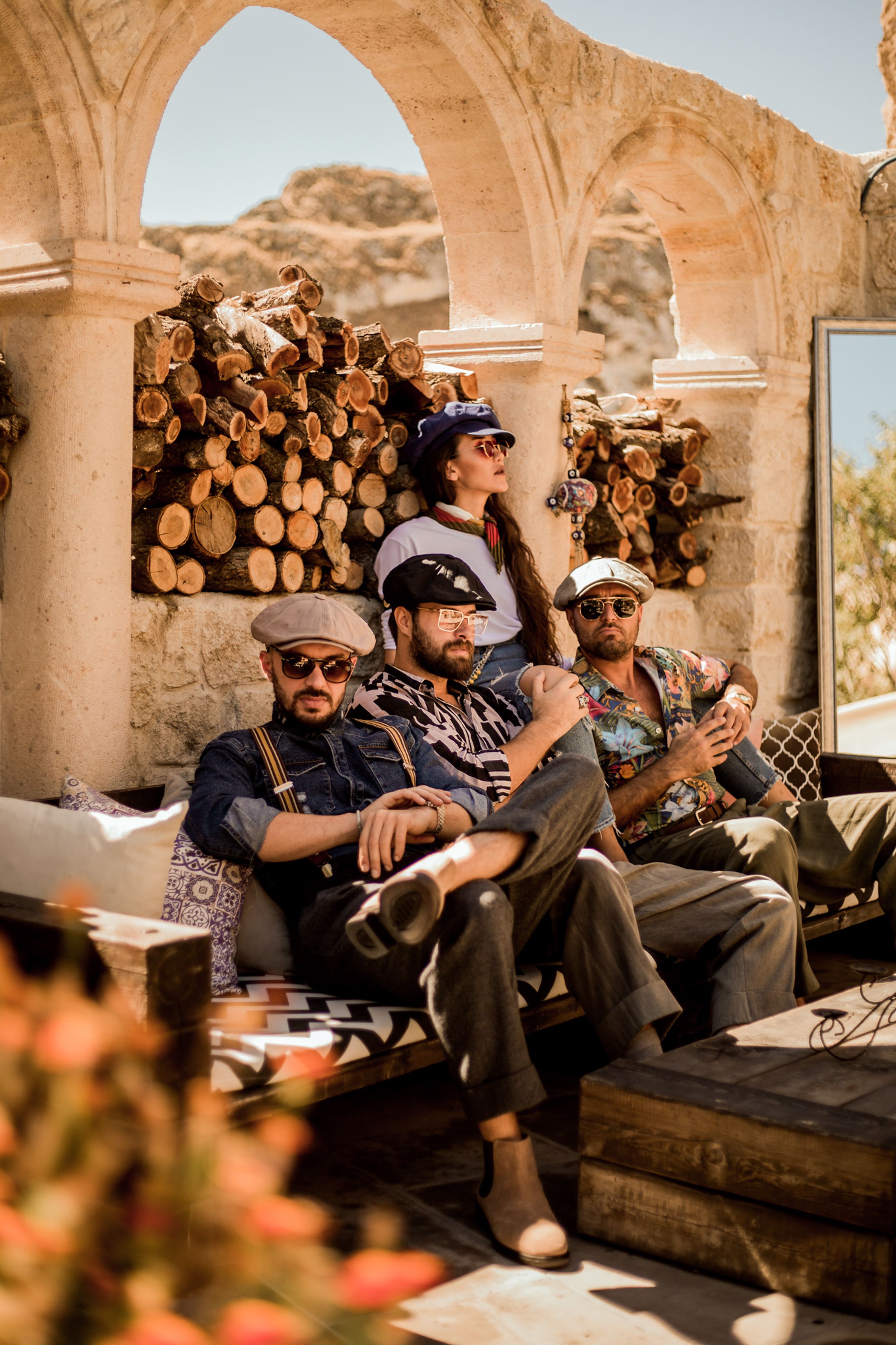 Four friends in vintage attire relaxing outdoors in Ürgüp, Türkiye with scenic backdrop.