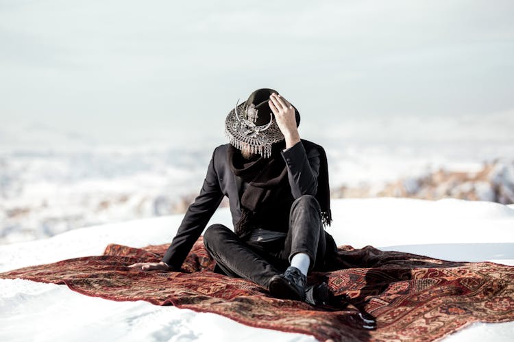 A Person In A Stylish Outfit Sitting On A Rug In The Snow