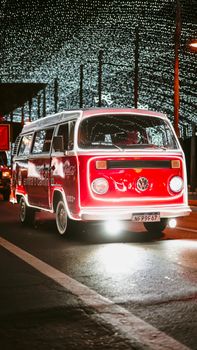 Bright red Volkswagen Kombi van under twinkling lights at night, evoking vintage charm.