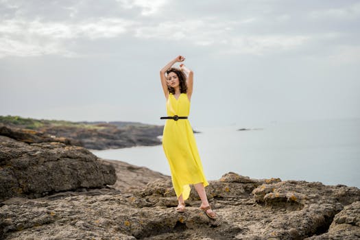 A woman in a yellow dress poses on rocky seaside terrain in Istanbul.