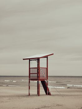 A solitary lifeguard tower stands quietly on a serene sandy beach under a muted sky.