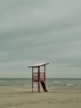 A lone lifeguard tower stands on a deserted beach under a cloudy sky, evoking a sense of isolation.