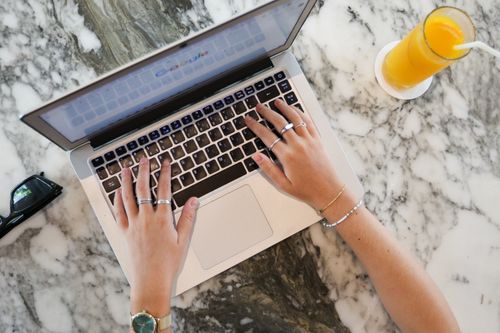 Free Hands typing on a laptop with orange juice on a marble surface, ideal for remote work themes. Stock Photo