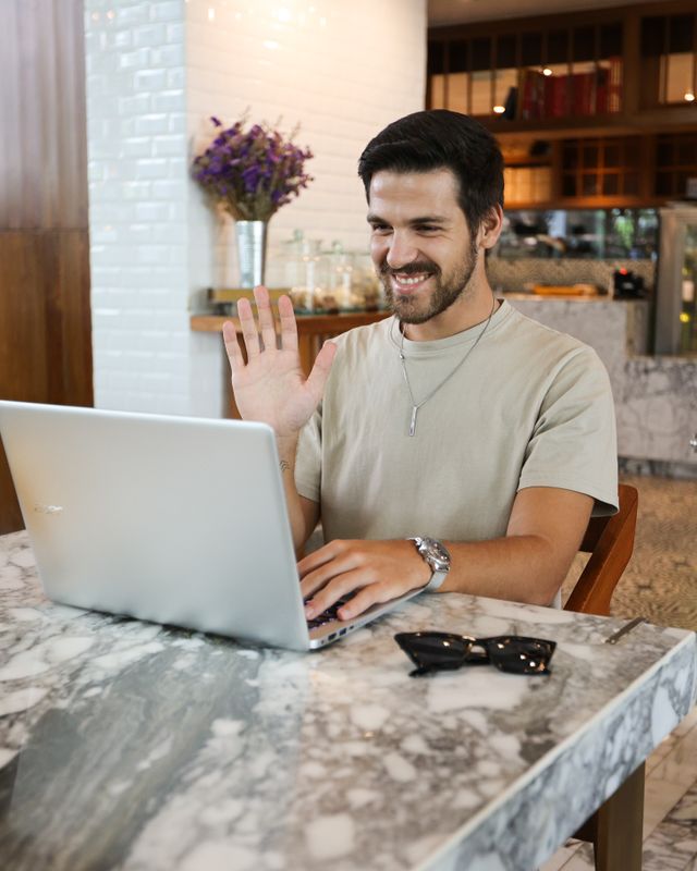 Retrato de um homem de barba, sorrindo diante do notebook em um café.