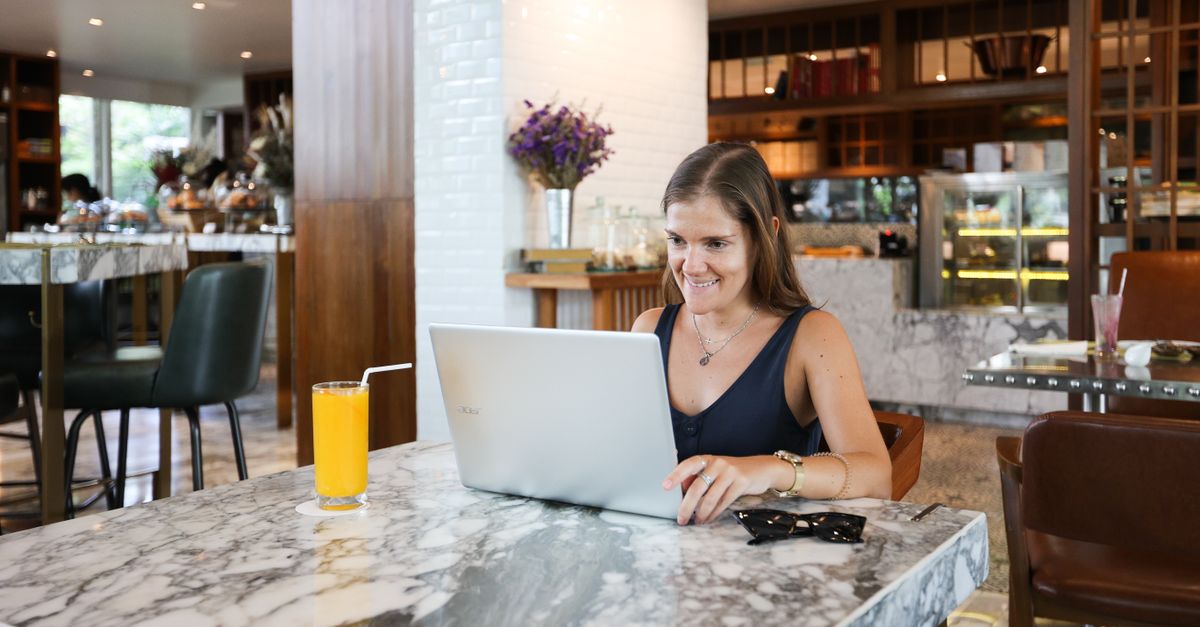Digital nomad working on a laptop at a beachside cafe with a passport and visa stamp visible
