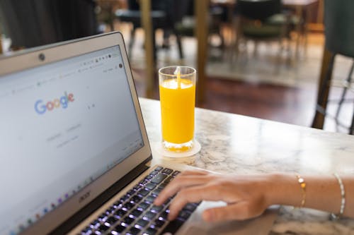 Free Woman Using a Computer Laptop Near a Glass of Juice Stock Photo