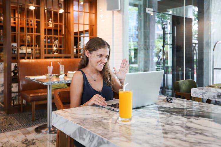 A Woman Waving While Sitting In Front Of A Laptop 