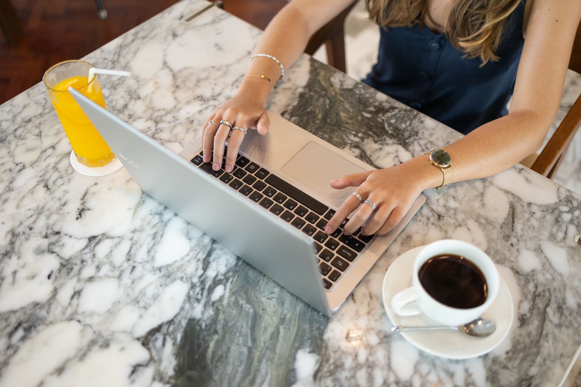 A woman working remotely on a laptop with coffee and orange juice on a marble table.