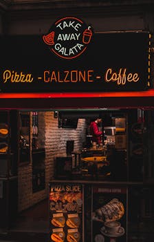 A cozy pizzeria entrance glowing with neon signs offering pizza, calzone, and coffee.