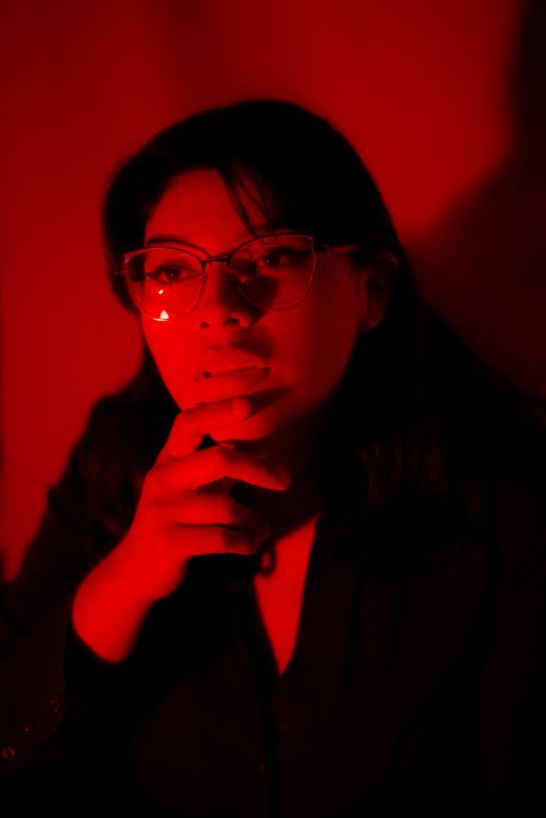 Free Thoughtful woman in red light with eyeglasses, conveying a dramatic mood. Stock Photo