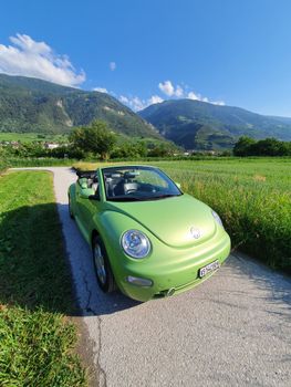 A retro green convertible parked on a picturesque mountain road under a clear blue sky.