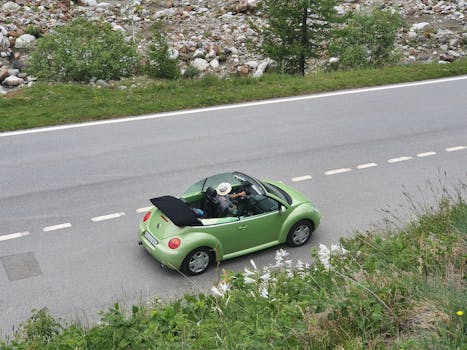 Aerial shot of a green convertible driving along a scenic road surrounded by nature.