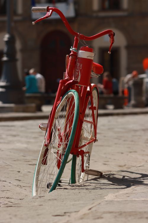 Free A vintage red bicycle parked on a sunny city street, capturing an urban lifestyle vibe. Stock Photo
