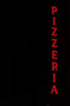 Vertical neon pizzeria sign glowing red against a black background, perfect for restaurant themes.