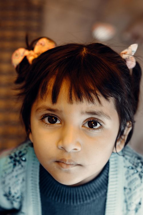 Free A close-up portrait of a cute child with bow hair ties, looking directly at the camera. Stock Photo