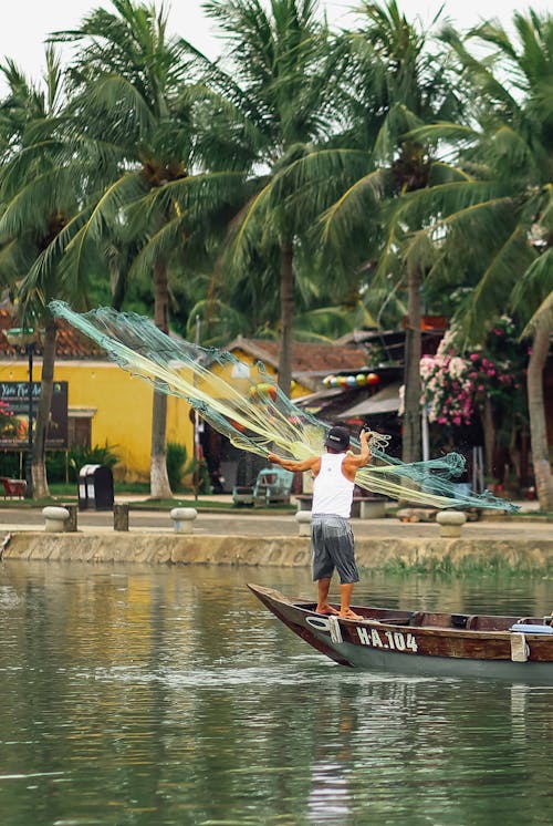 Man Standing on a Boat Throwing a Fishing Net
