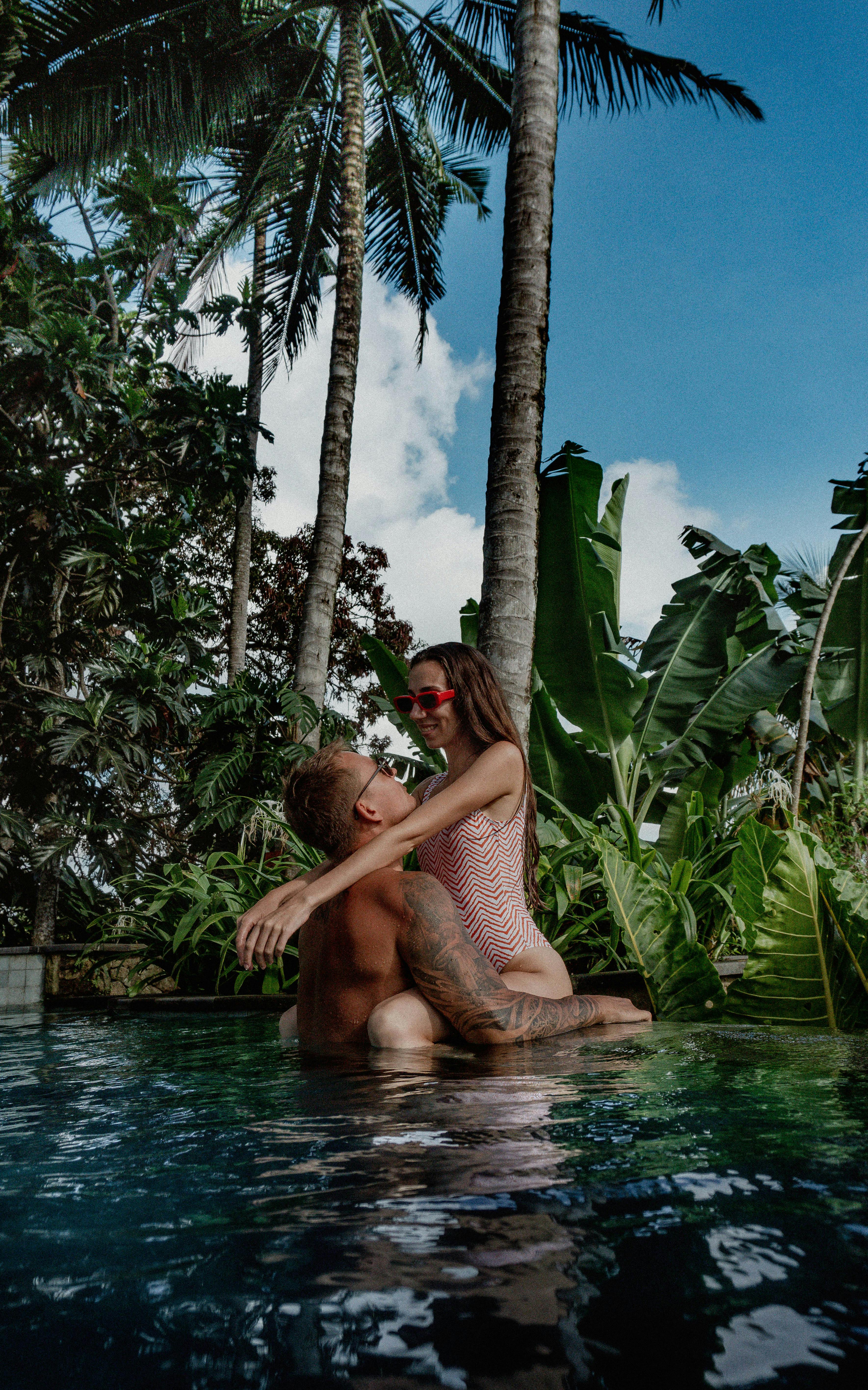 Woman and Man Posing under Trees around Swimming Pool · Free Stock Photo