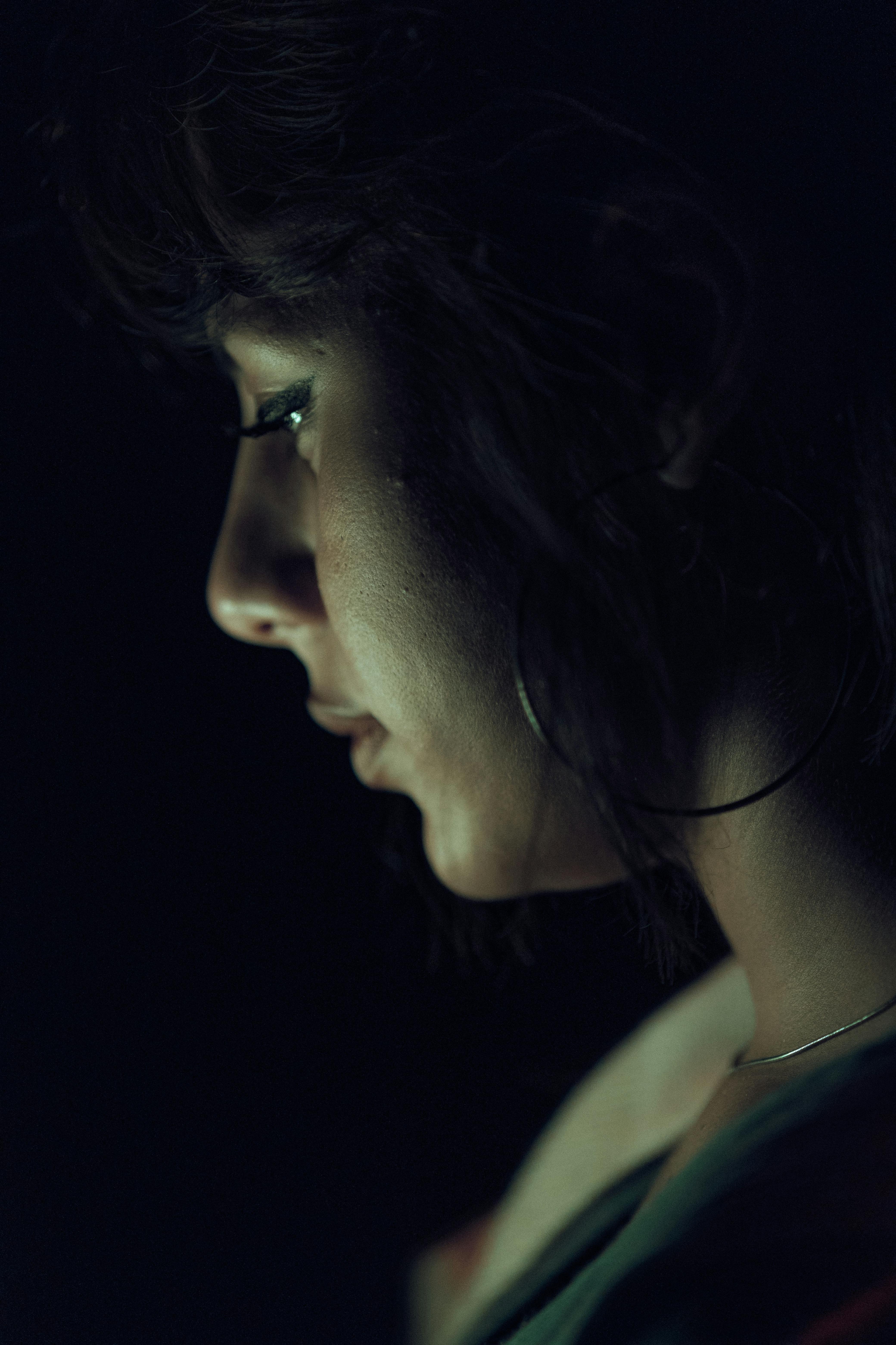 Moody side profile of a woman in low light, highlighting her features in a dark ambiance.