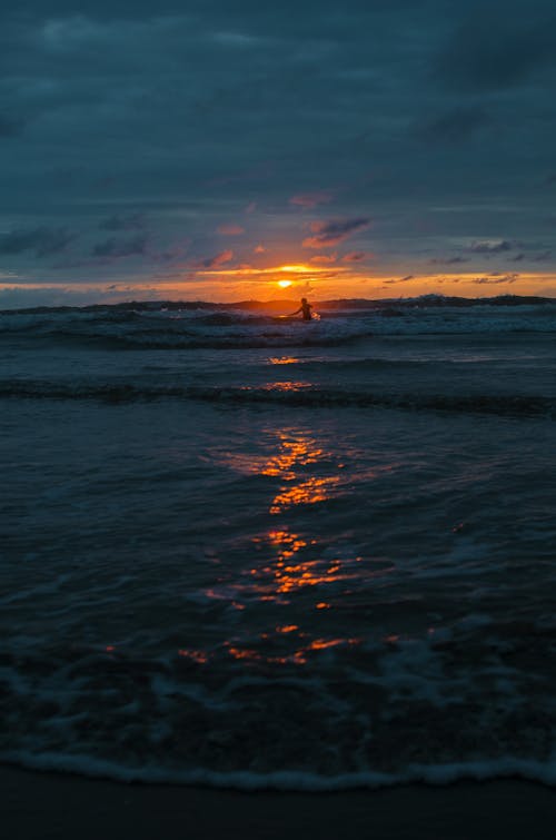 бесплатная Человек идет к пляжной волне во время золотого часа Стоковое фото