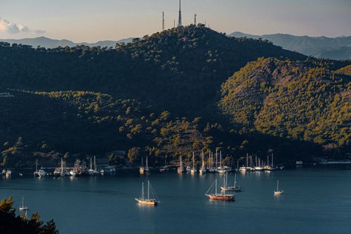 Free A tranquil bay surrounded by lush hills and distant mountains with sailing boats on calm waters. Stock Photo