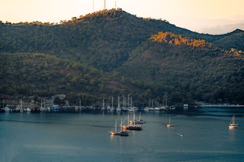 Free Peaceful harbor scene with sailboats moored under a golden sunset, nestled by lush hills. Stock Photo