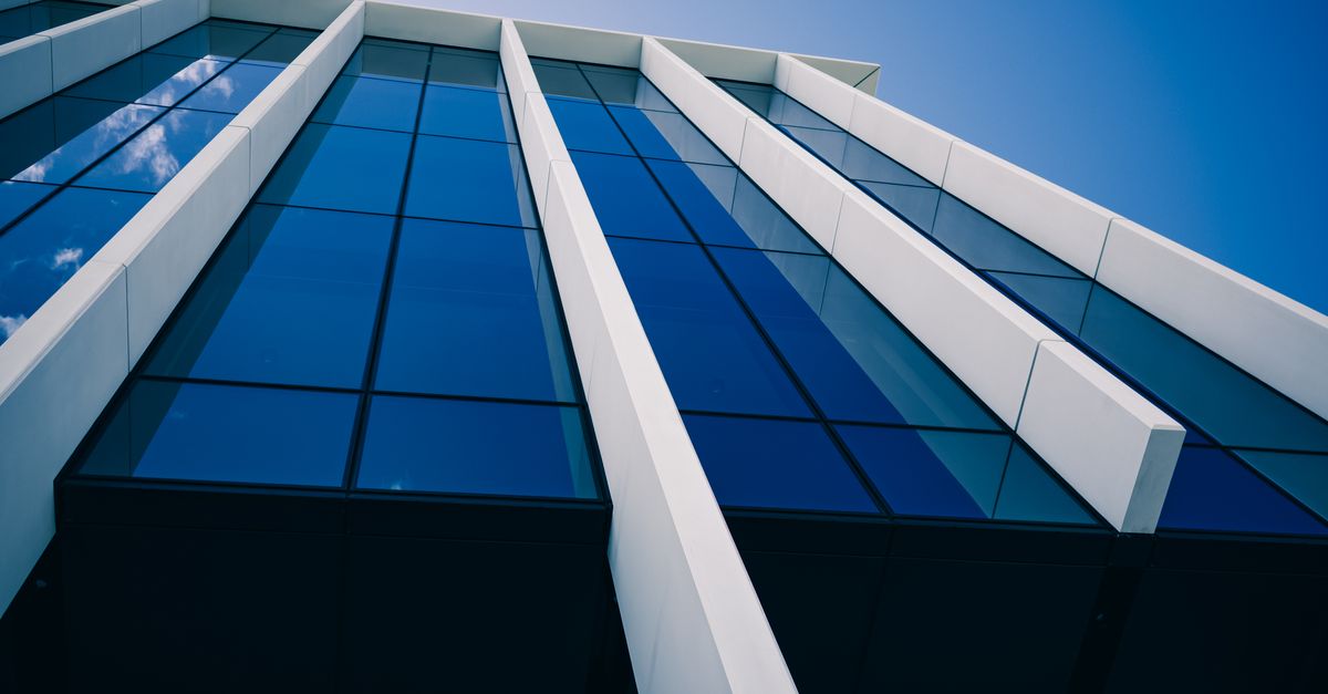 Low-angle view of a modern glass building against a clear blue sky, showcasing bold architectural lines.