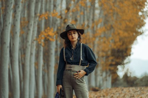 Free Woman in casual autumn attire stands among trees wearing a hat and suspenders. Stock Photo