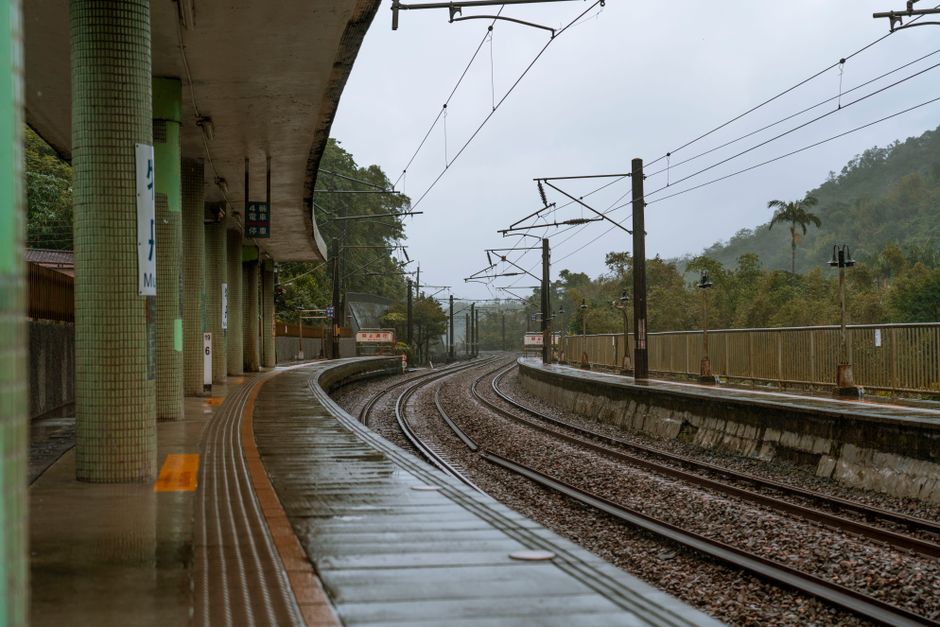 Empty train station platform in rainy weather, showcasing wet tracks and overcast skies.