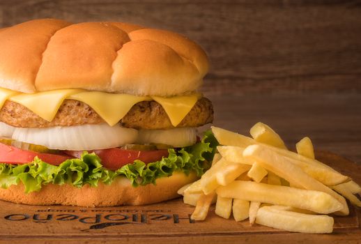 Close-up of a cheeseburger with lettuce, tomato, onion, and fries on a wooden surface.