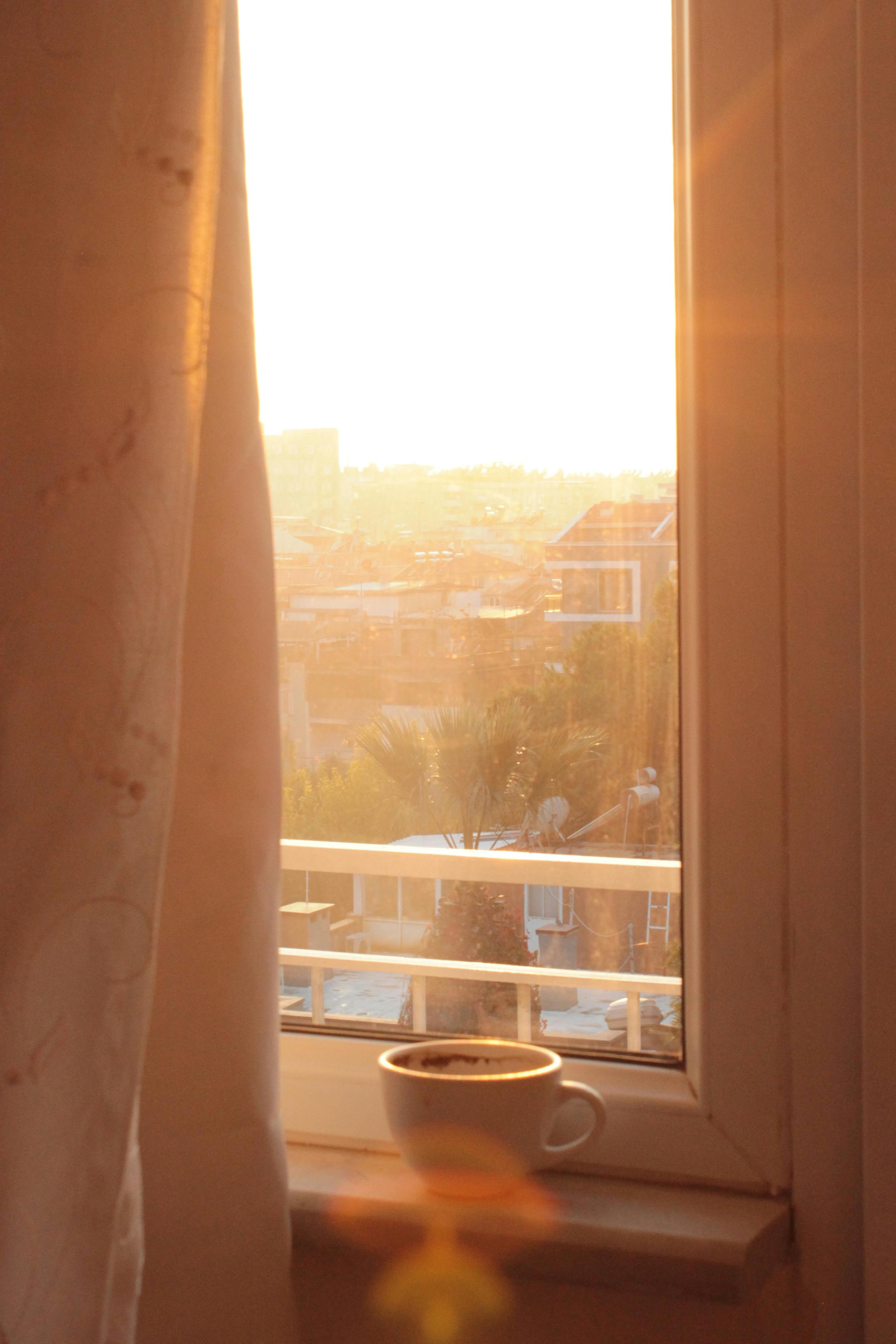 Sunlit room with a steaming cup of coffee on the windowsill, creating a calming morning scene.