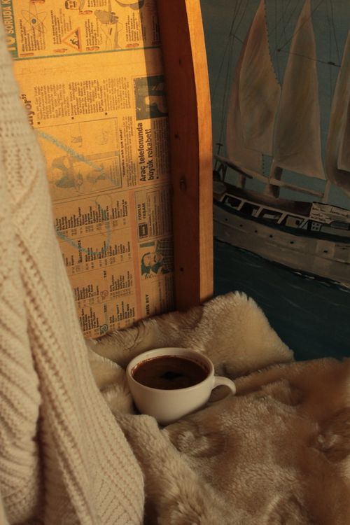 Free A steaming cup of coffee surrounded by cozy blankets and warm decor in a sunlit room. Stock Photo